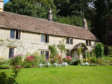 An English cottage built out of Cotswold stone with stone tiles on the roof, called slates, with a garden full of flowers and a grass lawn in the Cotswolds, England, UK., The Personal Property Shop, Bishops Stortford