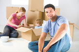 Young parents and their daughter sitting beside cardboard boxes. Young girl sitting in box. They're smiling. Focused on man who sitting in front., Man With Van South Hornchurch Ltd., Hornchurch