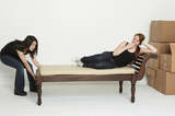 Young Asian woman pulls her room mate accross the room on a lounging sofa.  The lazy room mate pretends to be tired., Bow Man and Van Ltd., Bow
