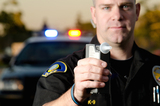 A police officer holding a breath test machine with his police car in the background. *the officer was blurred on purpose., Law Office of Attorney Robert H. Prince, Salem