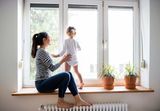 Beautiful young mother sitting on window sill with her cute little daughter looking out of window, Sunstopper Window Tinting, Melbourne