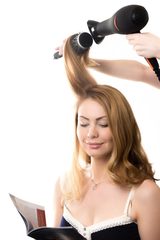 Portrait of young smiling gorgeous blond woman sitting at beauty salon reading fashion magazine, having her hair styled with hairdryer and round hairbrush, studio shot, isolated on white background, Ruby's Hair & Beauty Salon, London