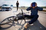 Bicyclists injured in a car accident lying down on the road and holding his head with helmet. A person who is driving car running to helps to injured man Los Angeles Bicycle Law, Bike Accident Attorney 3415 S Sepulveda Blvd, Ste 1100 