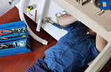 Plumber working on pipes under sink, Greg Mitchell Plumbing, Murgon